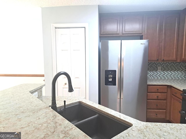 kitchen with stainless steel fridge, light stone counters, decorative backsplash, and a sink