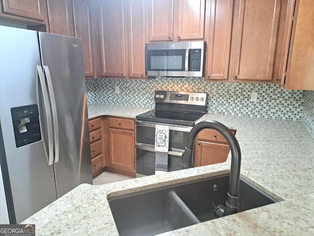 kitchen with a sink, tasteful backsplash, light stone countertops, and stainless steel appliances