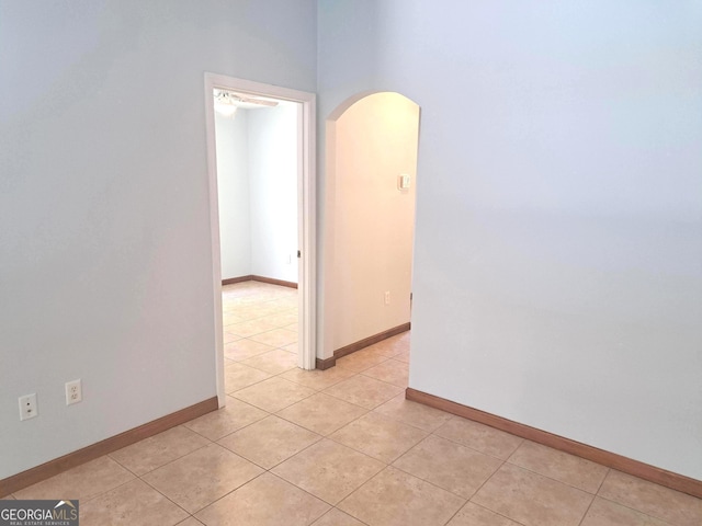 spare room featuring arched walkways, baseboards, and light tile patterned flooring