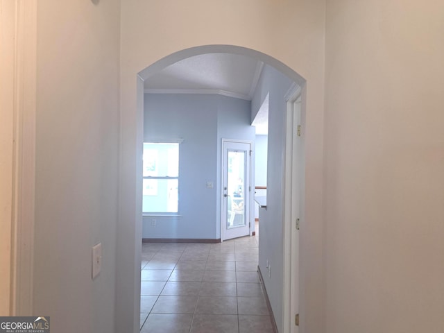 hallway with baseboards, ornamental molding, arched walkways, and light tile patterned floors