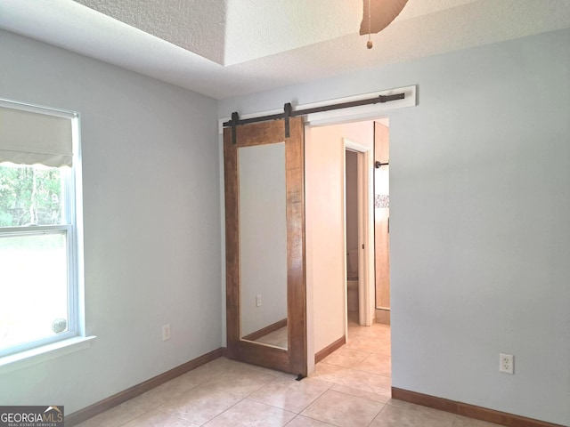 unfurnished room with light tile patterned floors, a textured ceiling, baseboards, and a barn door