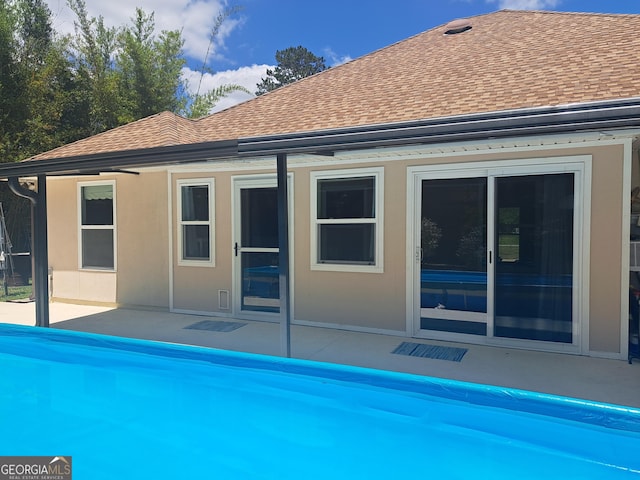 rear view of house with a patio, a shingled roof, stucco siding, and an outdoor pool