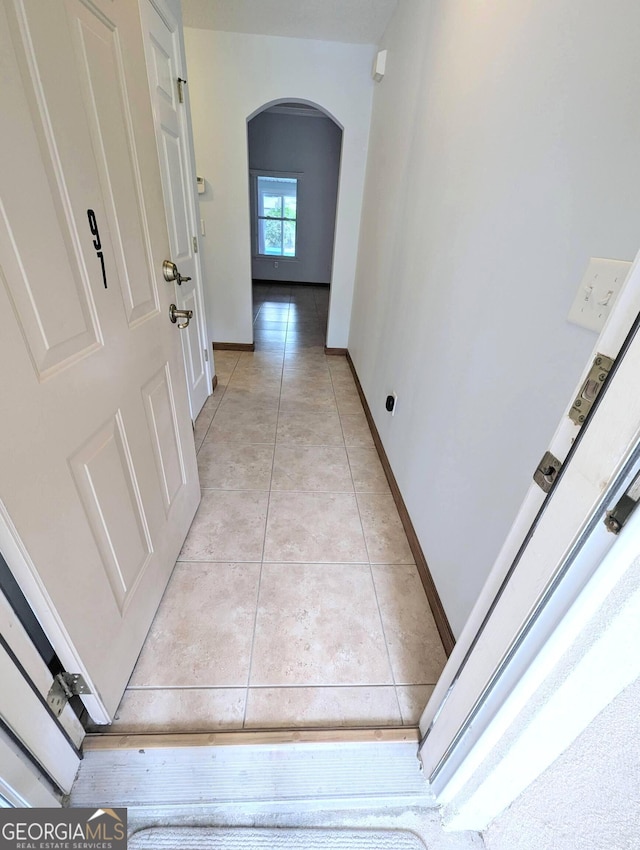 hallway featuring baseboards, arched walkways, and light tile patterned flooring