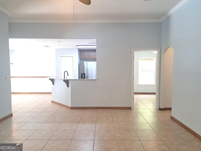 empty room featuring crown molding, light tile patterned flooring, ceiling fan, a sink, and arched walkways