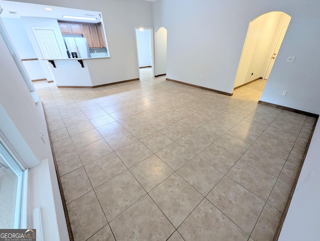 unfurnished living room featuring baseboards, arched walkways, and light tile patterned floors