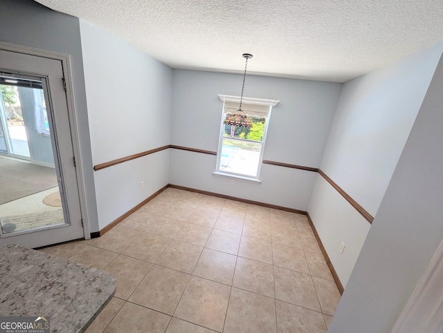 unfurnished dining area featuring baseboards, a textured ceiling, and light tile patterned floors