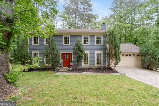colonial-style house featuring a garage, a chimney, concrete driveway, and a front yard