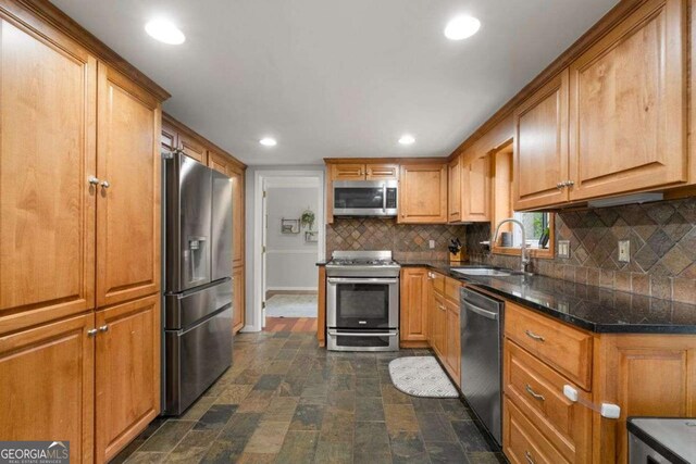 kitchen with brown cabinetry, backsplash, stone finish flooring, a sink, and stainless steel appliances