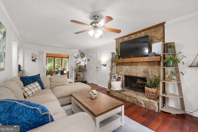 living room featuring crown molding, ceiling fan, a stone fireplace, baseboards, and wood finished floors