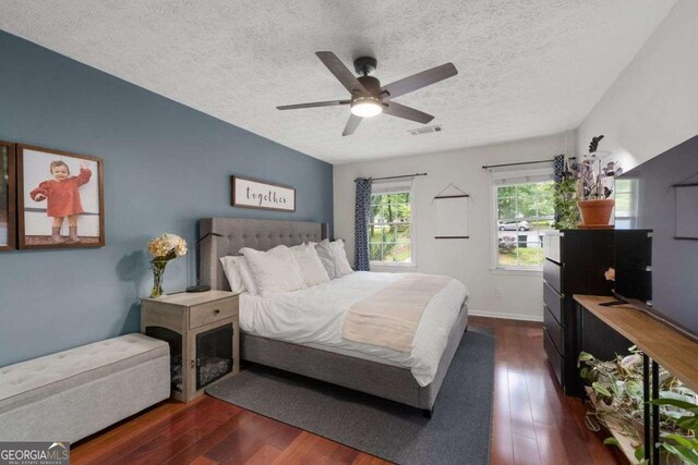 bedroom with a ceiling fan, a textured ceiling, visible vents, and dark wood-type flooring