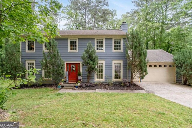 colonial home featuring a chimney, an attached garage, driveway, and a front yard