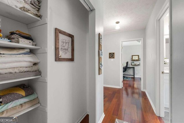 corridor featuring wood-type flooring, a textured ceiling, and baseboards