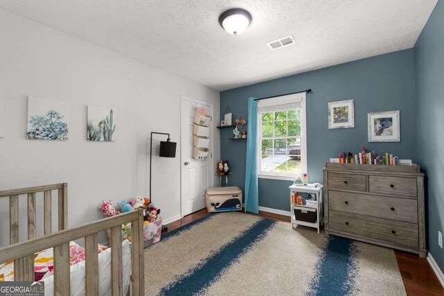bedroom with visible vents, baseboards, a textured ceiling, and wood finished floors