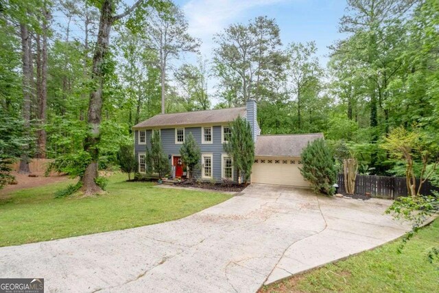 colonial-style house with a garage, a front lawn, fence, a chimney, and driveway