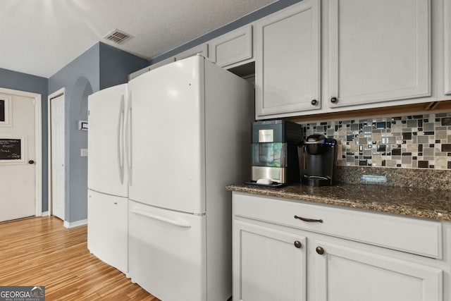 224 Pine Bluff Dr, Kingsland, GA 31548 - kitchen with visible vents, freestanding refrigerator, light wood-type flooring, dark stone countertops, and backsplash