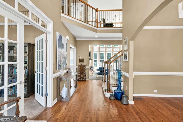 foyer featuring baseboards, french doors, wood finished floors, and a towering ceiling