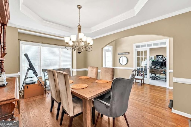 dining room with light wood-style floors, arched walkways, a raised ceiling, an inviting chandelier, and ornamental molding