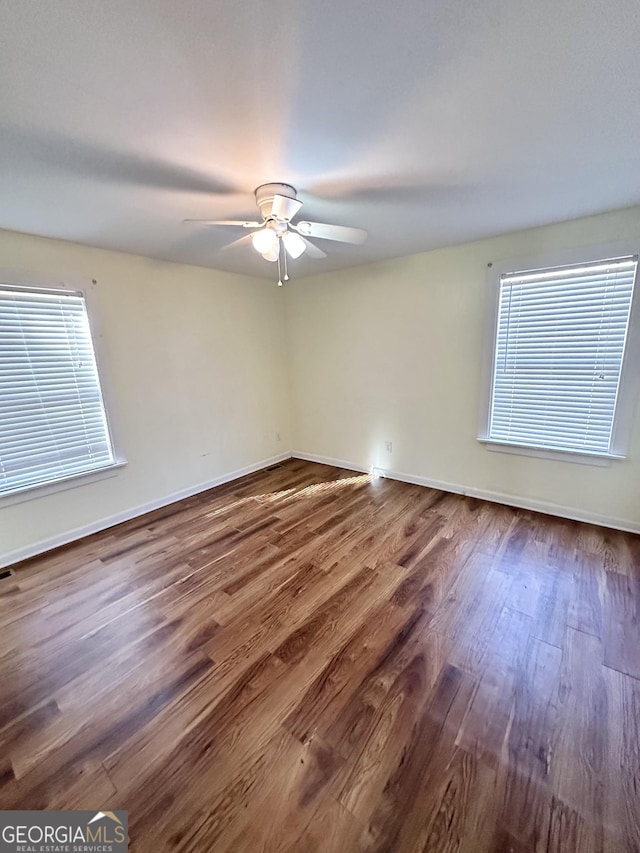 spare room featuring baseboards, a ceiling fan, wood finished floors, and a wealth of natural light