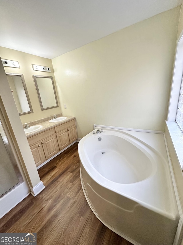 full bath featuring double vanity, a sink, a bath, and wood finished floors