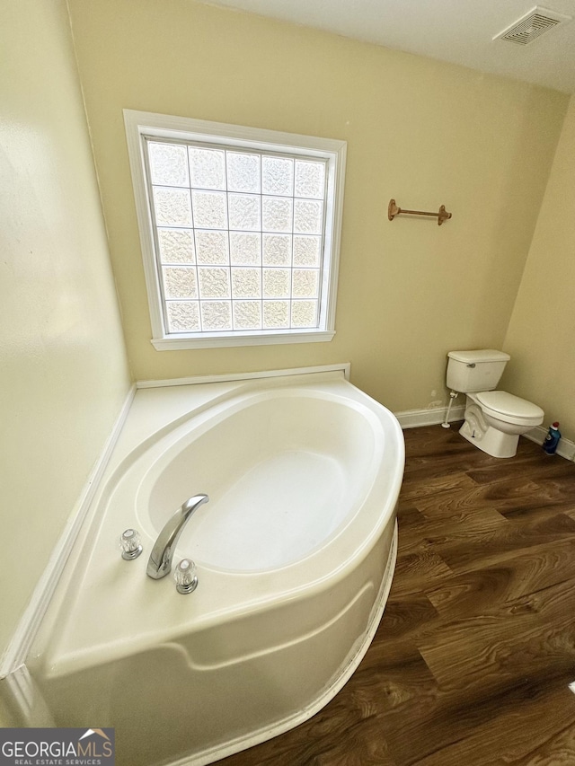 full bathroom featuring wood finished floors, toilet, a bath, and visible vents