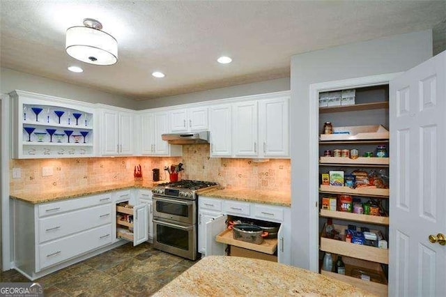 kitchen featuring light stone counters, white cabinetry, under cabinet range hood, and range with two ovens