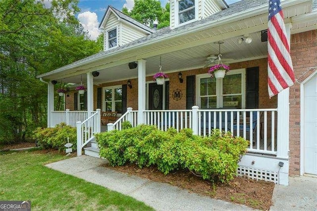 doorway to property featuring a porch, a ceiling fan, roof with shingles, and brick siding