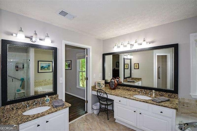 full bathroom featuring a textured ceiling, visible vents, two vanities, and a sink