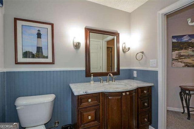 half bathroom with toilet, wainscoting, and vanity