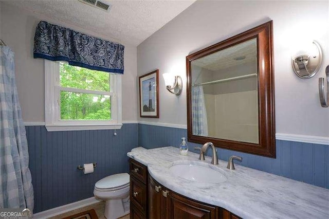 bathroom with wainscoting, toilet, a textured ceiling, and visible vents