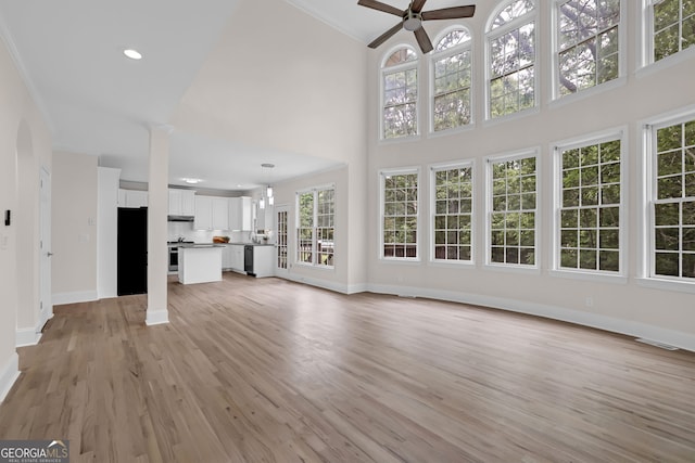 unfurnished living room with a towering ceiling, light wood-style flooring, baseboards, and ceiling fan