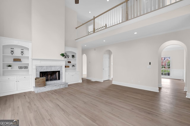 unfurnished living room with built in features, a fireplace, light wood-style flooring, arched walkways, and a high ceiling