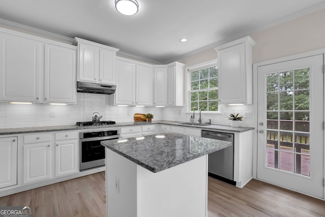 kitchen with under cabinet range hood, light wood finished floors, a sink, white cabinetry, and appliances with stainless steel finishes