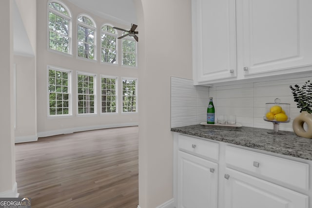 bar with wood finished floors, baseboards, ceiling fan, backsplash, and a dry bar