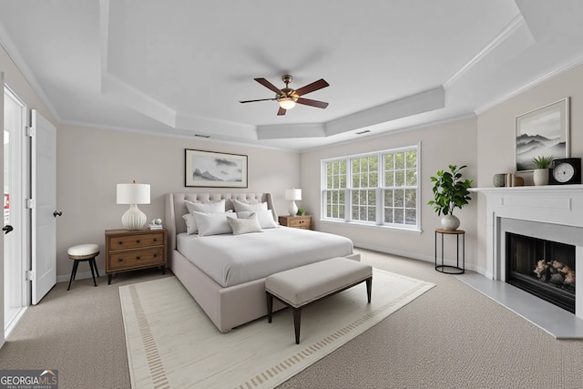 bedroom featuring a tray ceiling, crown molding, light carpet, and a fireplace