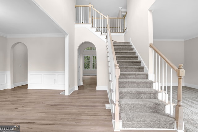 stairway with ornamental molding, wood finished floors, and arched walkways