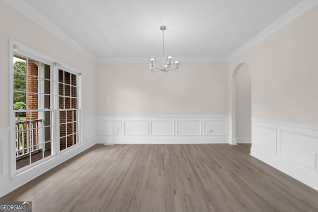 unfurnished dining area featuring ornamental molding, wainscoting, a chandelier, wood finished floors, and arched walkways