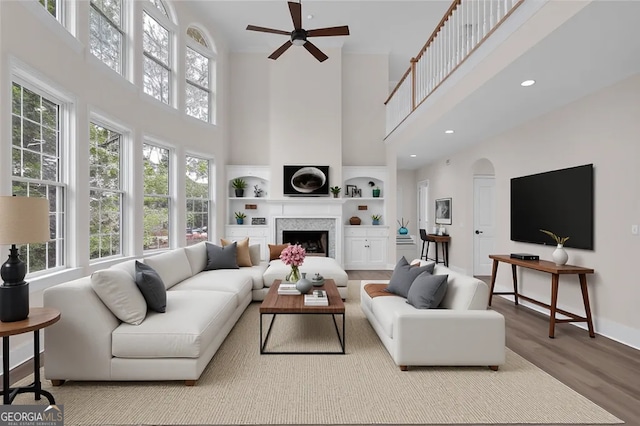 living room featuring wood finished floors, built in features, ceiling fan, arched walkways, and a high ceiling