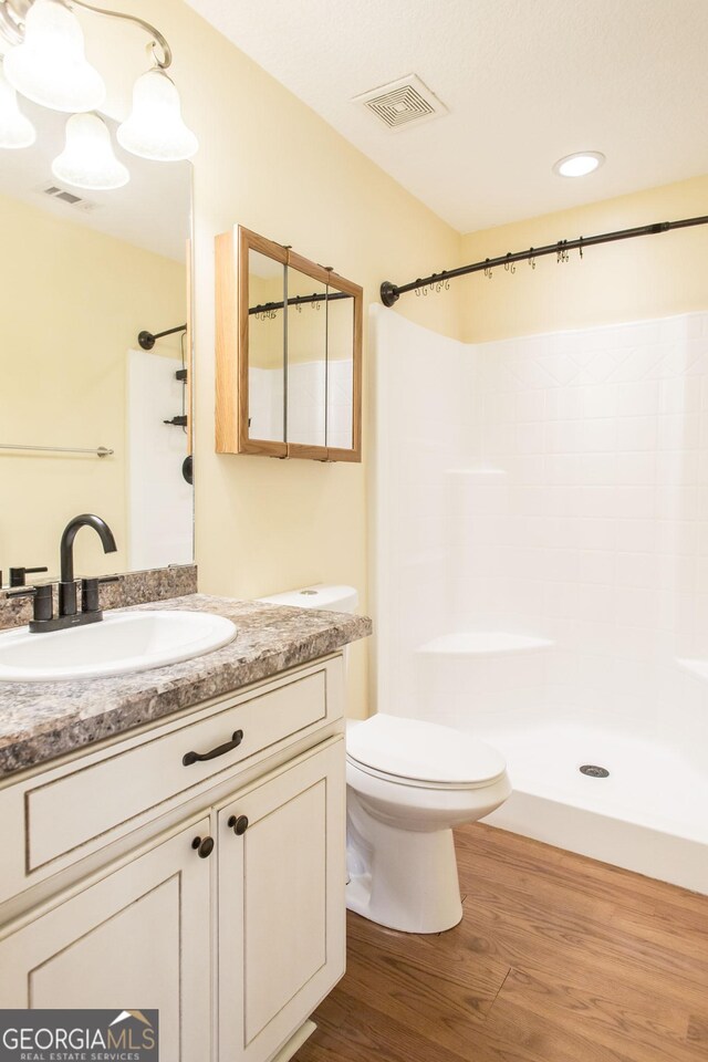 bathroom featuring walk in shower, vanity, toilet, wood finished floors, and visible vents