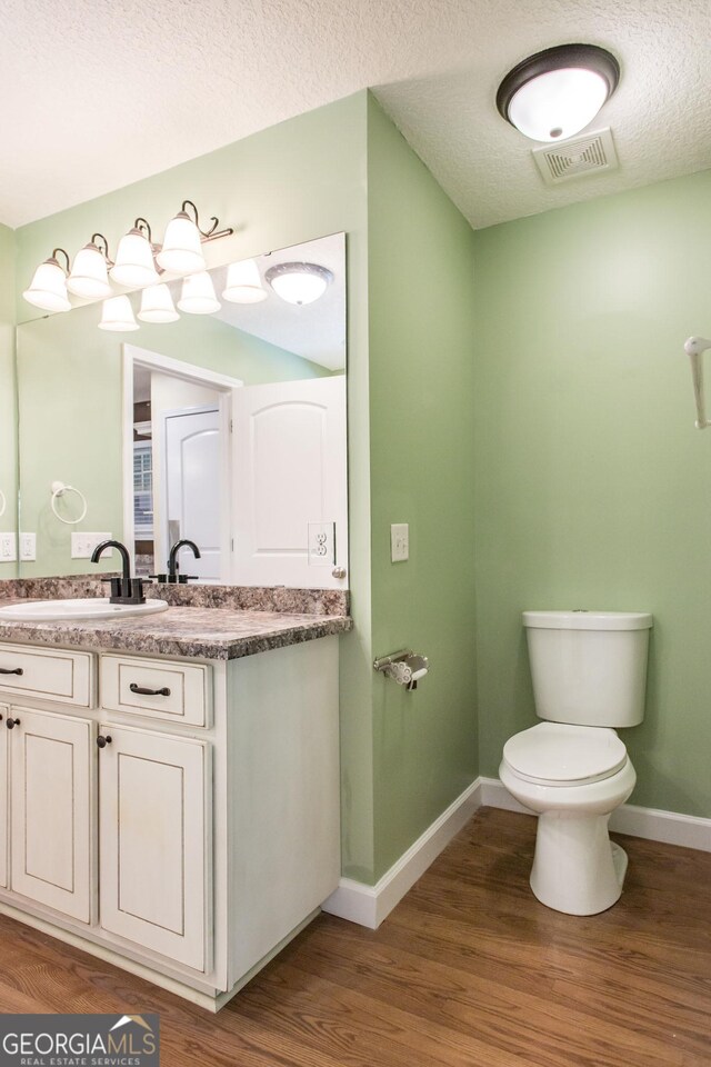 bathroom with visible vents, vanity, wood finished floors, toilet, and baseboards