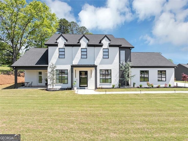 modern inspired farmhouse with a shingled roof, stucco siding, a patio area, and a front lawn