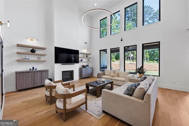 living room featuring a glass covered fireplace, baseboards, light wood-type flooring, and a towering ceiling