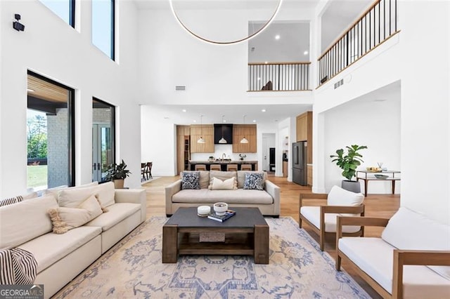 living room featuring visible vents, light wood-type flooring, and a towering ceiling