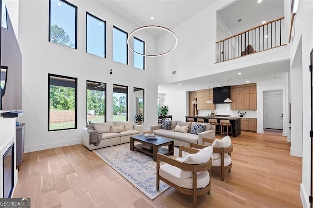 living room with a high ceiling, baseboards, and light wood-type flooring
