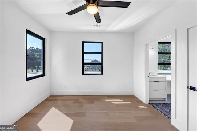 empty room featuring ceiling fan, visible vents, a healthy amount of sunlight, and wood finished floors