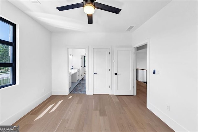 unfurnished bedroom featuring baseboards, ensuite bathroom, wood finished floors, and ceiling fan