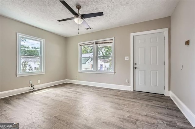 interior space featuring a textured ceiling, baseboards, wood finished floors, and visible vents