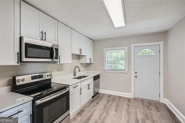 kitchen with white cabinetry, a sink, baseboards, stainless steel appliances, and light wood-style flooring