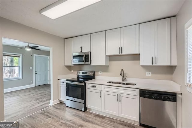 kitchen with appliances with stainless steel finishes, a sink, light wood finished floors, light countertops, and white cabinetry