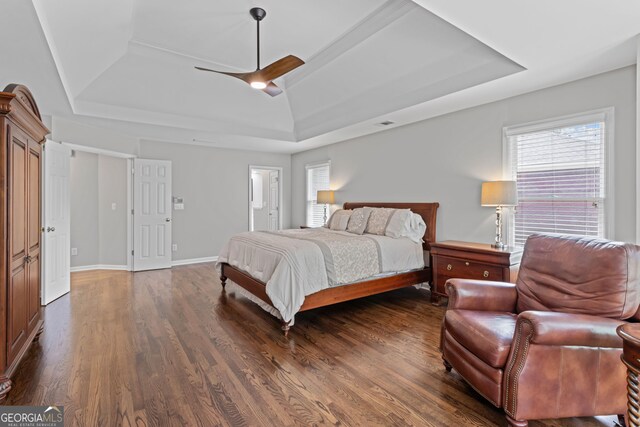bedroom featuring baseboards, dark wood-type flooring, a raised ceiling, a ceiling fan, and ensuite bath