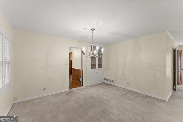 unfurnished dining area featuring light colored carpet, a notable chandelier, a wainscoted wall, baseboards, and visible vents